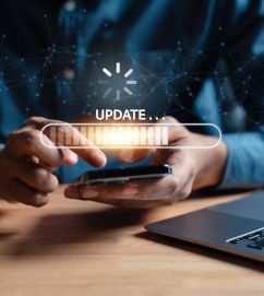 Man sieht die Hände eines Mannes, die ein Handy umfassen. Auf dem Bild ist ein Symbol mit dem Hinweis "Update".